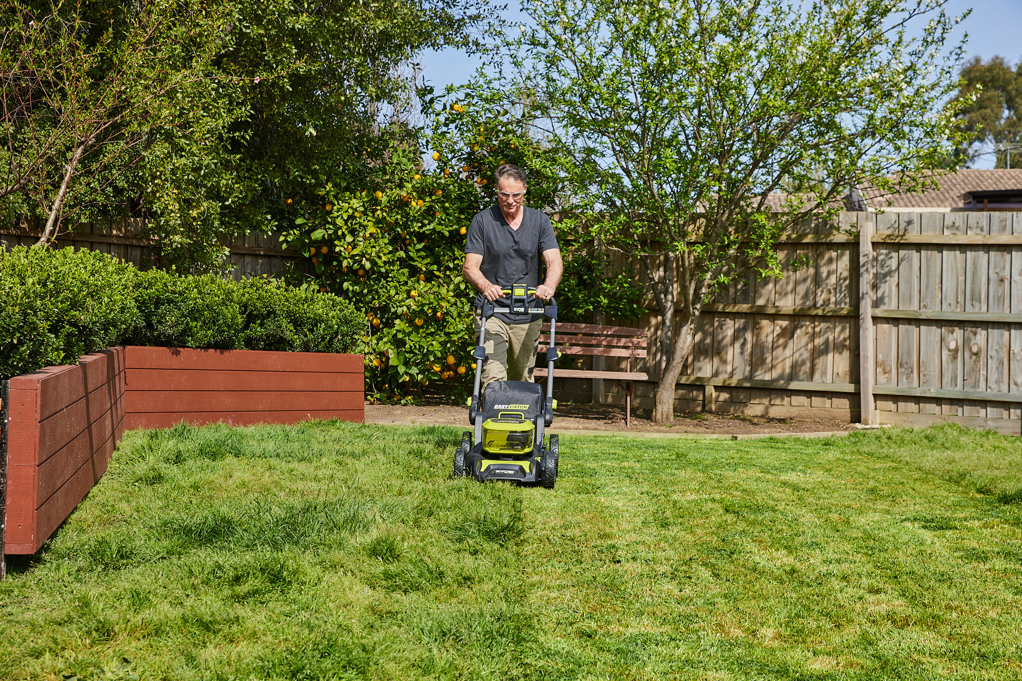 A man uses a Ryobi lawn mower to trim the grass in his backyard