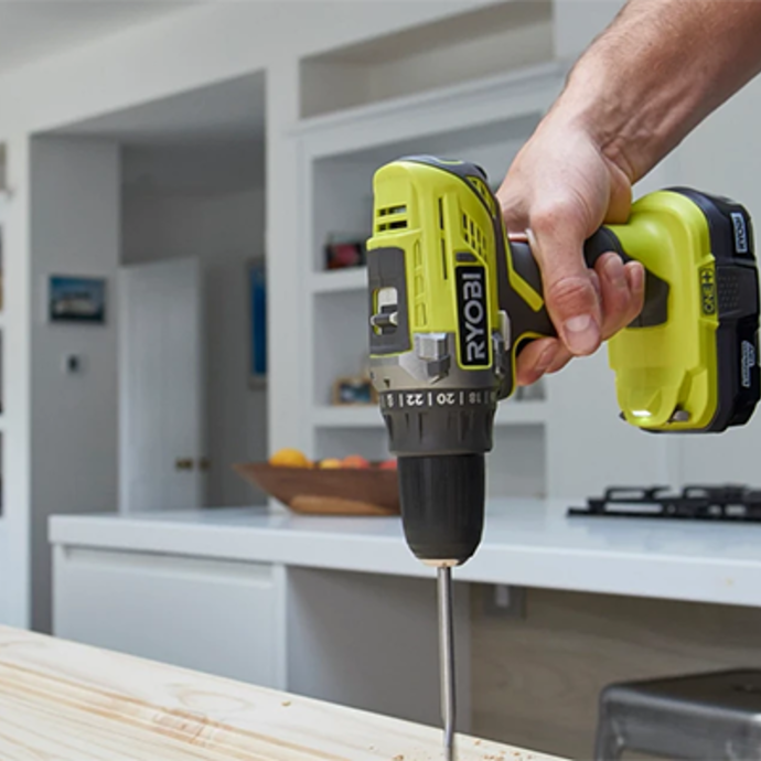 A person uses a RYOBI Drill Driver to drill into the kitchen bench